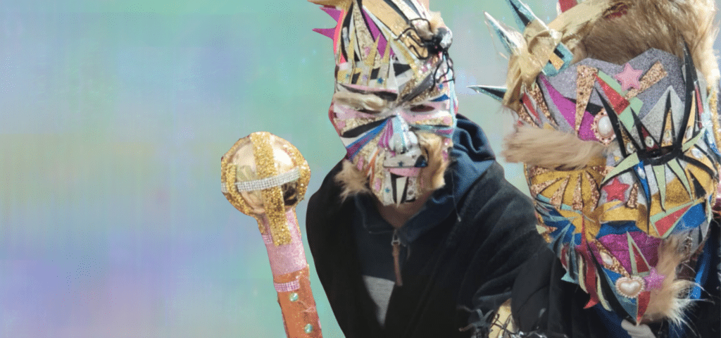 Zwei Personen tragen aufwendig gestaltete, bunte Masken mit Glitzer und Stacheln – Kunstmasken von Johann, entstanden während seiner Psychosen bei paranoider Schizophrenie