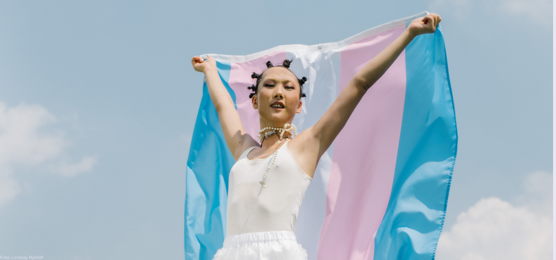 Person mit weißem armellosen Oberteil hält rosa-blau gestreiften Stoff hinter sich nach oben.