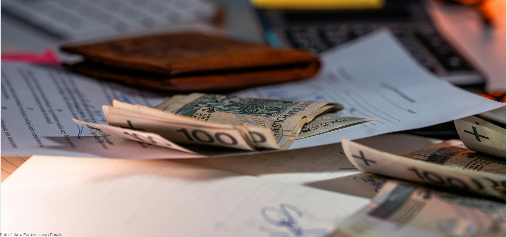 Gefaltete Geldscheine auf einem Tisch, dahinter liegt eine Geldbörse.