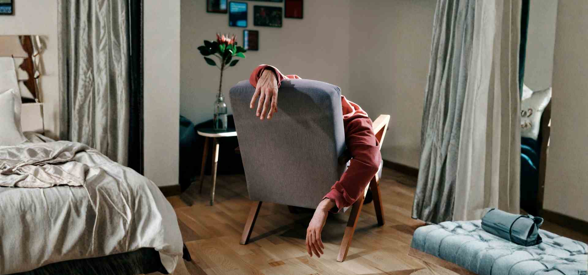 Erschöpfte Person über Sessel – psychischer Zusammenbruch und Suche nach Therapie Person hängt erschöpft mit hängenden Armen über die Rückenlehne eines Sessels im Schlafzimmer – Symbolbild für psychische Erschöpfung und den Zusammenbruch, der den Weg zur KI-Therapie auslöst