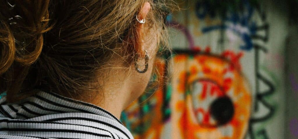 Junge Frau von hinten mit Ohrringen vor buntem Graffiti-Hintergrund